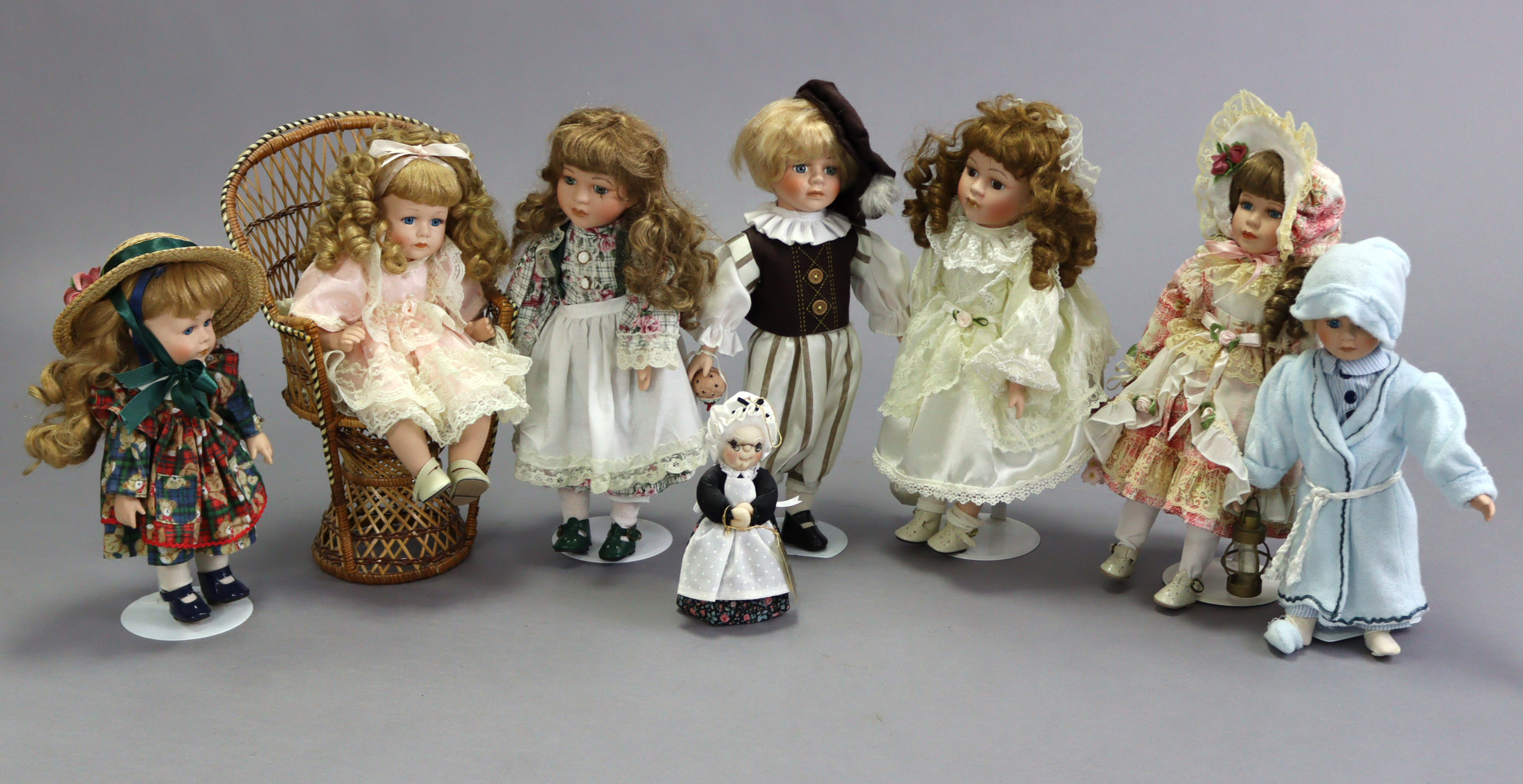 Eight modern bisque-head costume dolls of various sizes, each with stand, one with wicker chair.