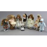 Eight modern bisque-head costume dolls of various sizes, each with stand, one with wicker chair.