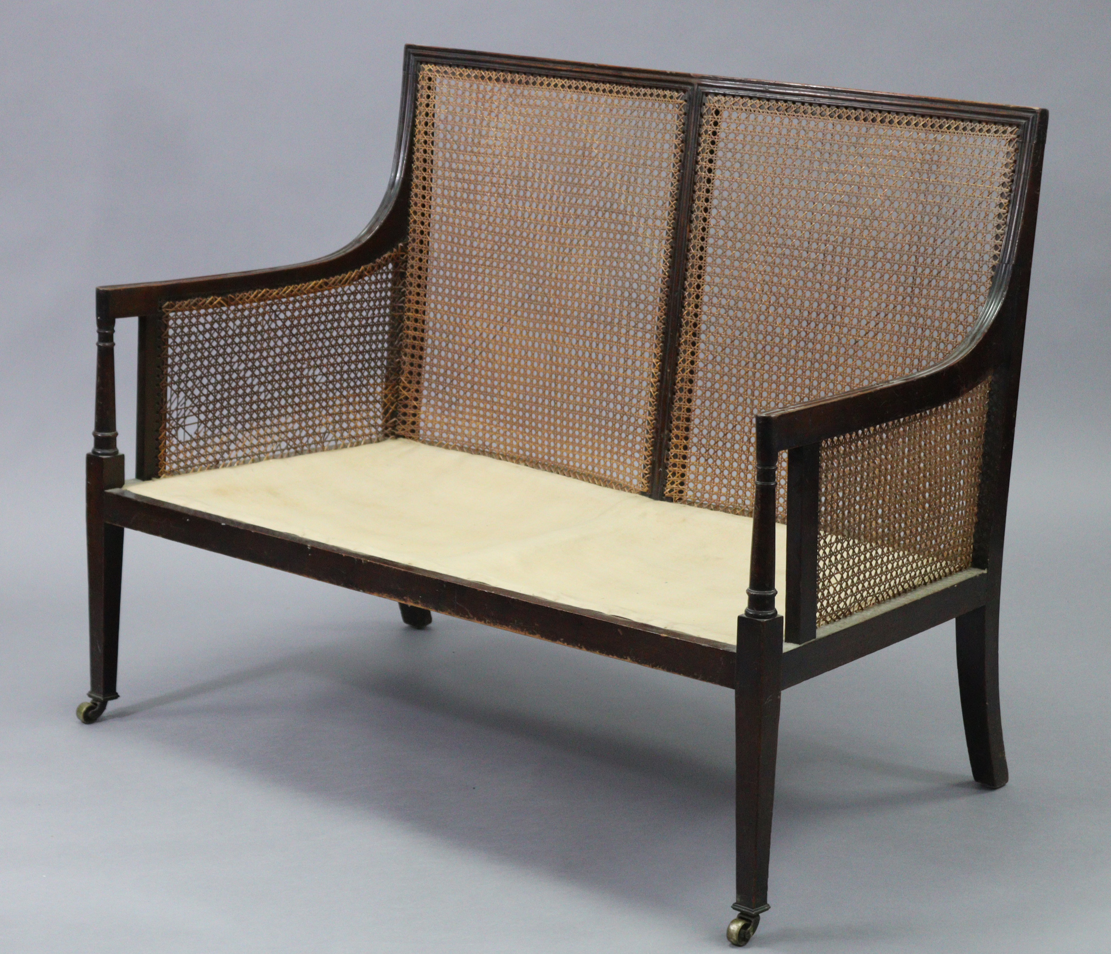 A mahogany two seater bergere settee in the late George III style, with moulded edges, turned arm