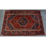 A Persian rug of deep red ground with central lozenge motif surrounded by repeating geometric