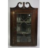 A George III mahogany hanging corner cabinet, the swan-neck pediment with brass foliate roundels