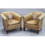 A pair of brass-studded tan leather tub-shaped easy chairs, each on four short square tapered legs.