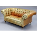 A chesterfield-style buttoned tan leather two-seater settee, on short turned legs with brass