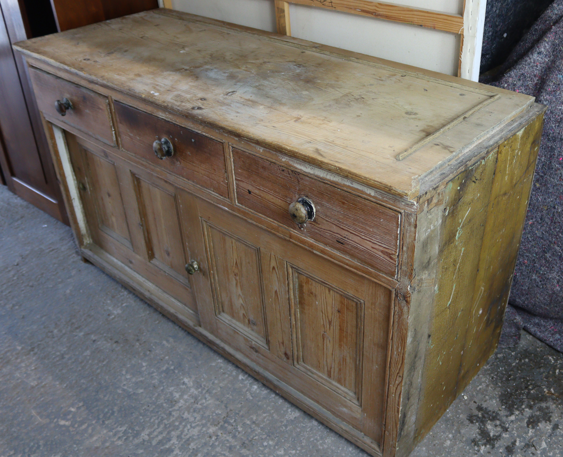 A pine dresser base, fitted three frieze drawers above cupboard enclosed by pair of sliding panel