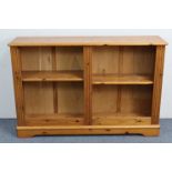 A pine low standing open bookcase with two adjustable shelves, & on shaped plinth base, 47” wide x