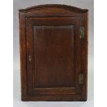 An 18th century oak hanging corner cupboard, with arched cornice above three shaped shelves