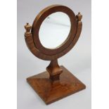 A mahogany veneered circular shaving mirror with bevelled plate & half-round support, on a shaped