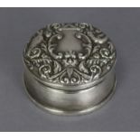 A silver trinket box, the circular hinged lid with embossed mask, bird, & leaf-scroll decoration,