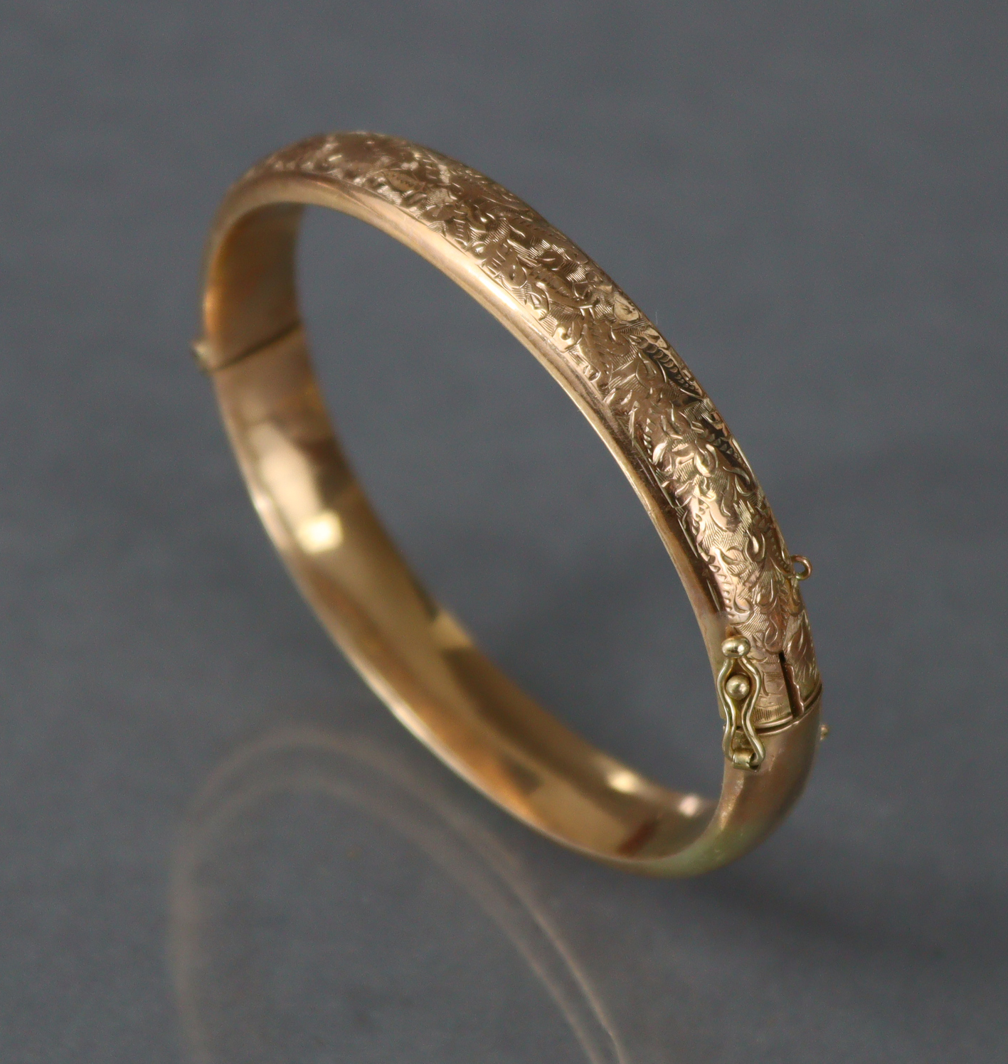 A 9ct. gold stiff hinged bangle with engraved decoration to one half; Chester hallmarks for 1912. (