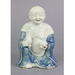A Chinese Dehua porcelain figure of a smiling immortal, seated, holding precious objects, with
