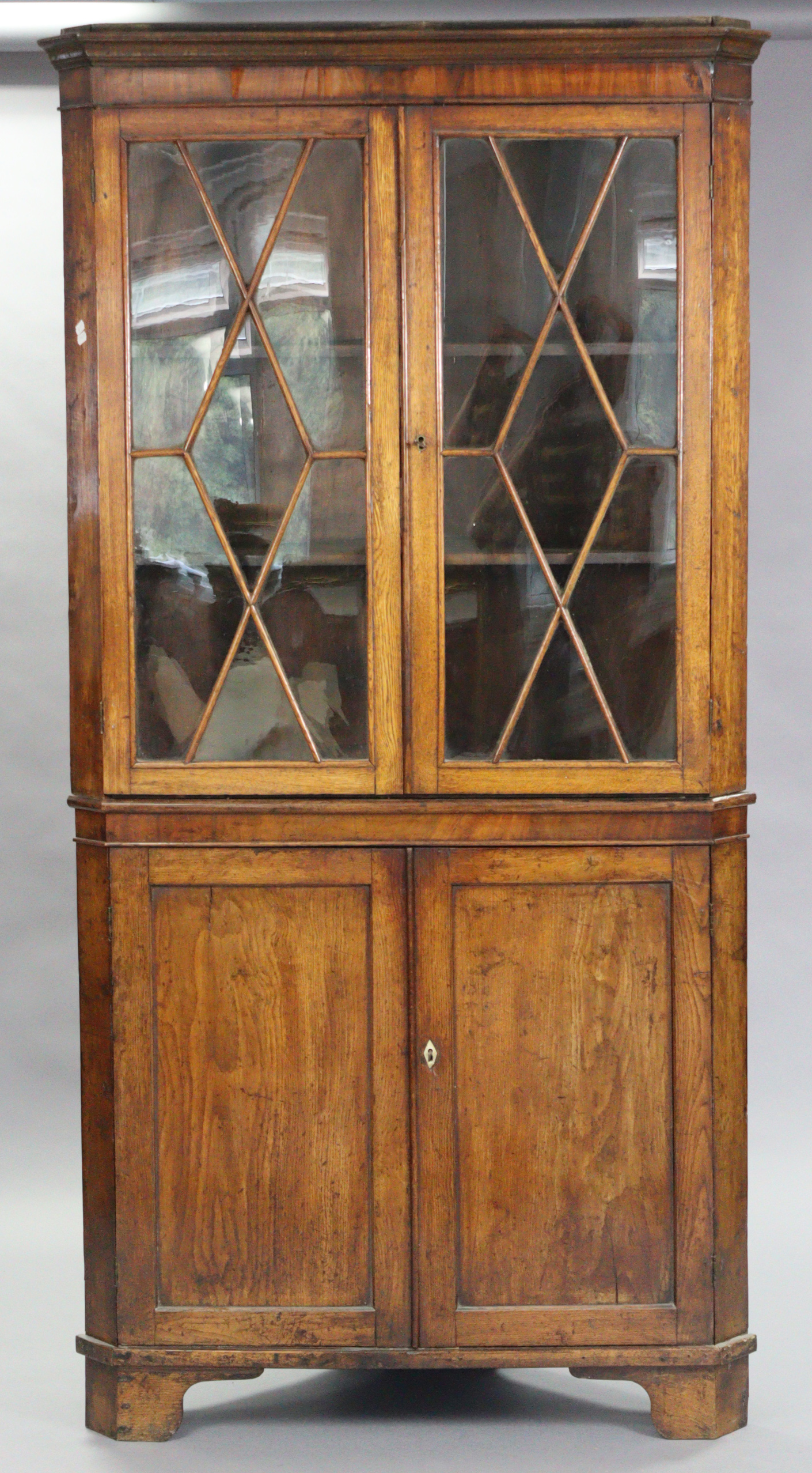 A late 18th century oak standing corner cabinet, the upper part fitted two shelves enclosed by