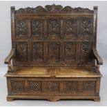 A late Victorian oak box-seat settle, with profusely carved stylised foliate decoration in the
