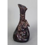 A Japanese aubergine-glazed pottery vase in the form of Daikoku seated on a giant sack; 10¼” high.