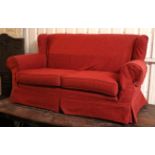 A wing-back three-seater settee upholstered crimson material, with loose cushions to seat, & on
