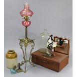 A Victorian-style brass oil table lamp with cranberry-tinted glass reservoir, 27” high; a glass