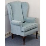 A wing-back armchair upholstered pale blue material, & on short cabriole legs