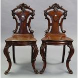 A pair of Victorian mahogany hall chairs with carved & pierced backs, hard seats, & on carved