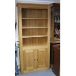 A modern light oak tall standing open bookcase with three adjustable shelves above cupboard enclosed