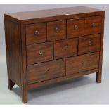 A contemporary teak chest fitted with an arrangement of seven small drawers with brass ring handles,