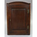 An early 18th century oak hanging corner cupboard, with arched cornice above three shaped shelves