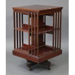A late Victorian inlaid-mahogany square revolving bookcase of three tiers, with rail sides, & on cas
