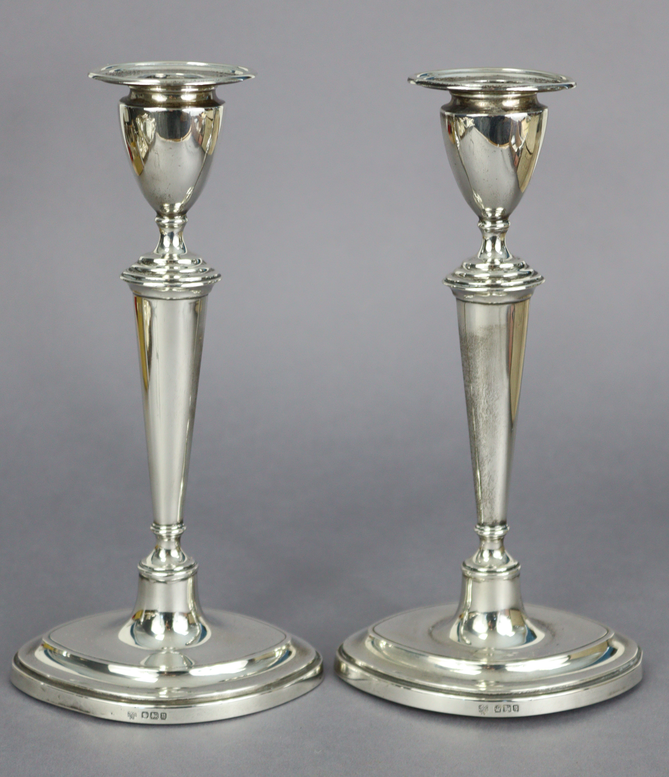 A pair of George V silver candlesticks in the late 18th century style, with vase-shaped nozzles,