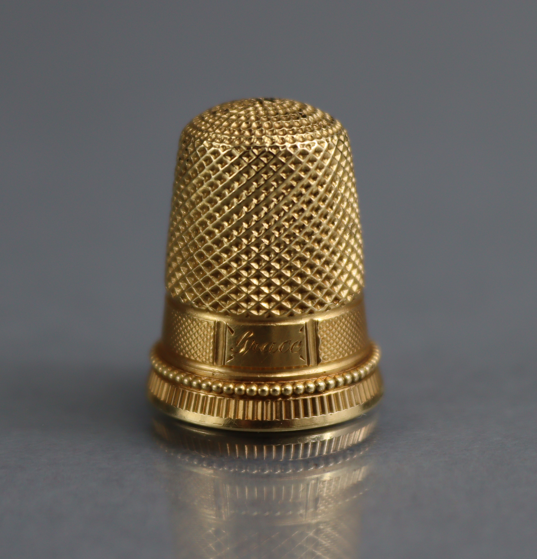 A GOLD THIMBLE with engraved inscription “Grace”, ¾” high, un-marked (6.8gm); in TIFFANY & Co.