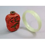 A Chinese pale jade bangle, 3” diam.; together with a red lacquered snuff bottle with mountainous