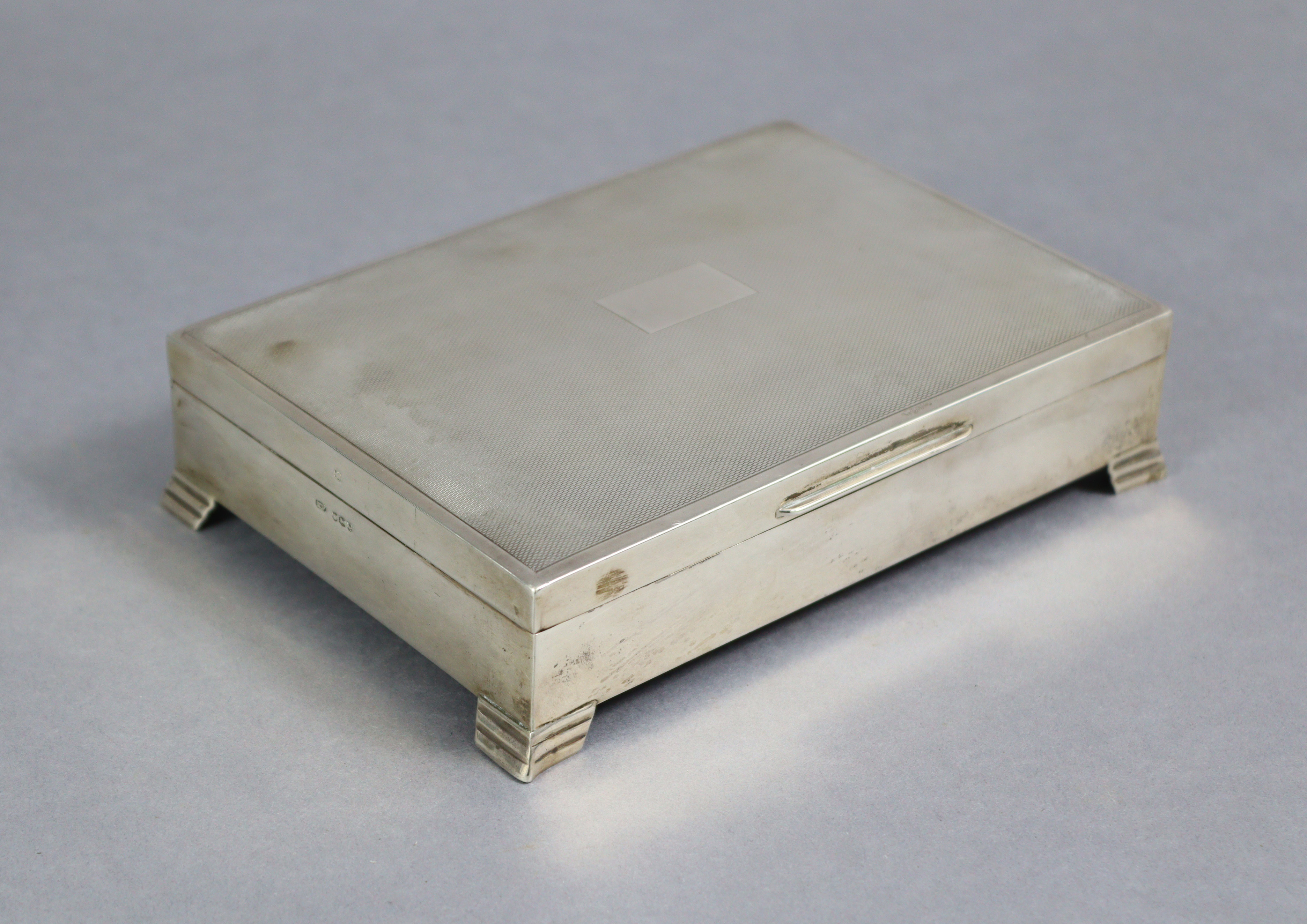 A silver cigarette box with engine-turned hinged cover, plain sides, wood-lined interior, & on