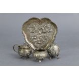 An eastern white metal three-piece condiment set on lobed heart-shaped tray, with repoussé