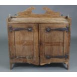 An Arts & Crafts oak hanging wall cabinet in the Liberty style, with shaped surmount above a pair of