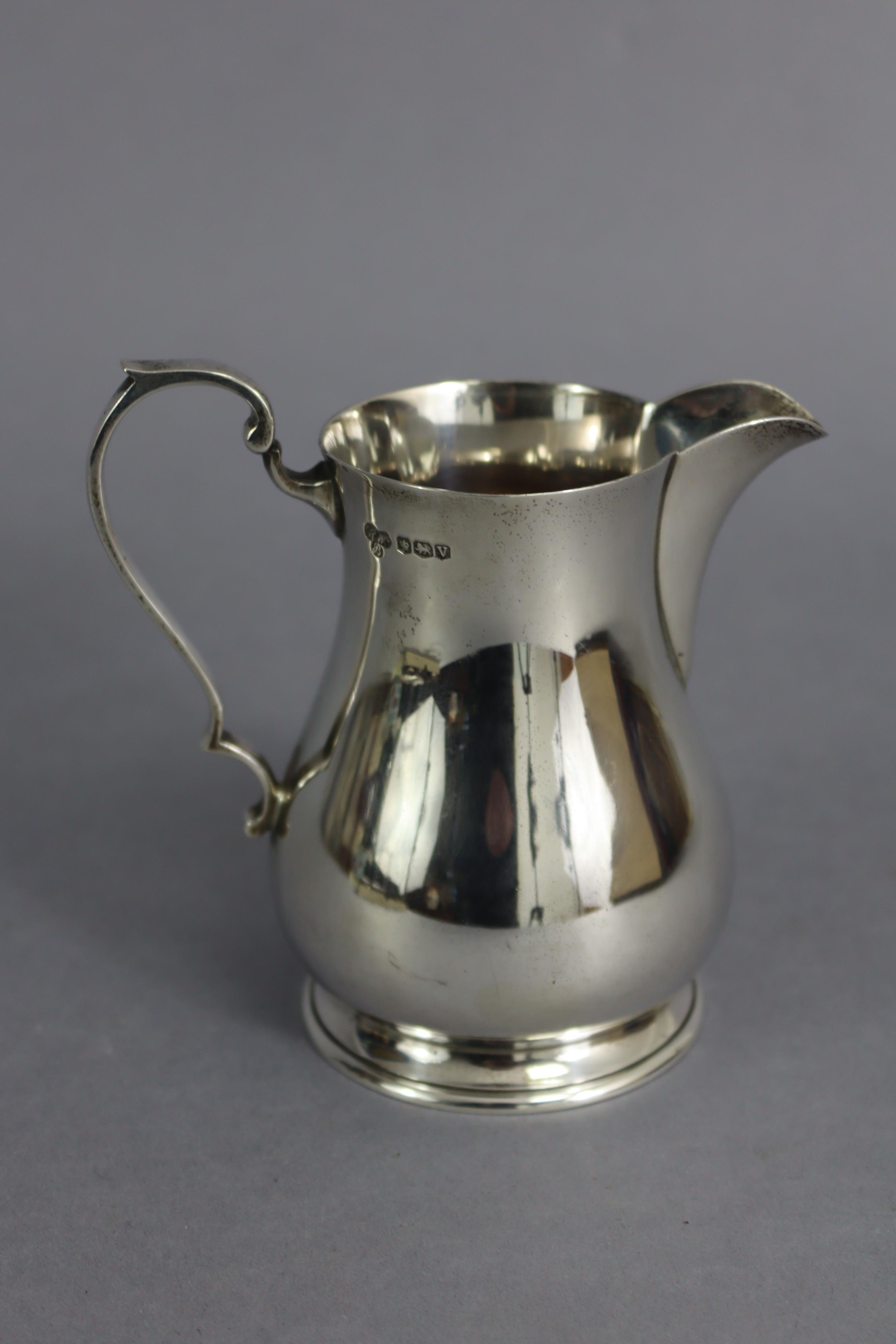 A George V silver baluster milk jug in the mid-18th century style, with scroll handle & on spread