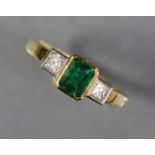 An emerald & diamond ring, the rectangular centre stone weighing approx. 0.6 carat, flanked by a