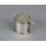 A George III silver drum-shaped mustard pot with pierced shell thumb-piece to the flat hinged lid,