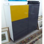 An Ikea white laminate cupboard with two pairs of grey and mustard coloured doors,