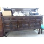 A 1930s stained oak sideboard with a panelled upstand, over three frieze drawers and three doors,