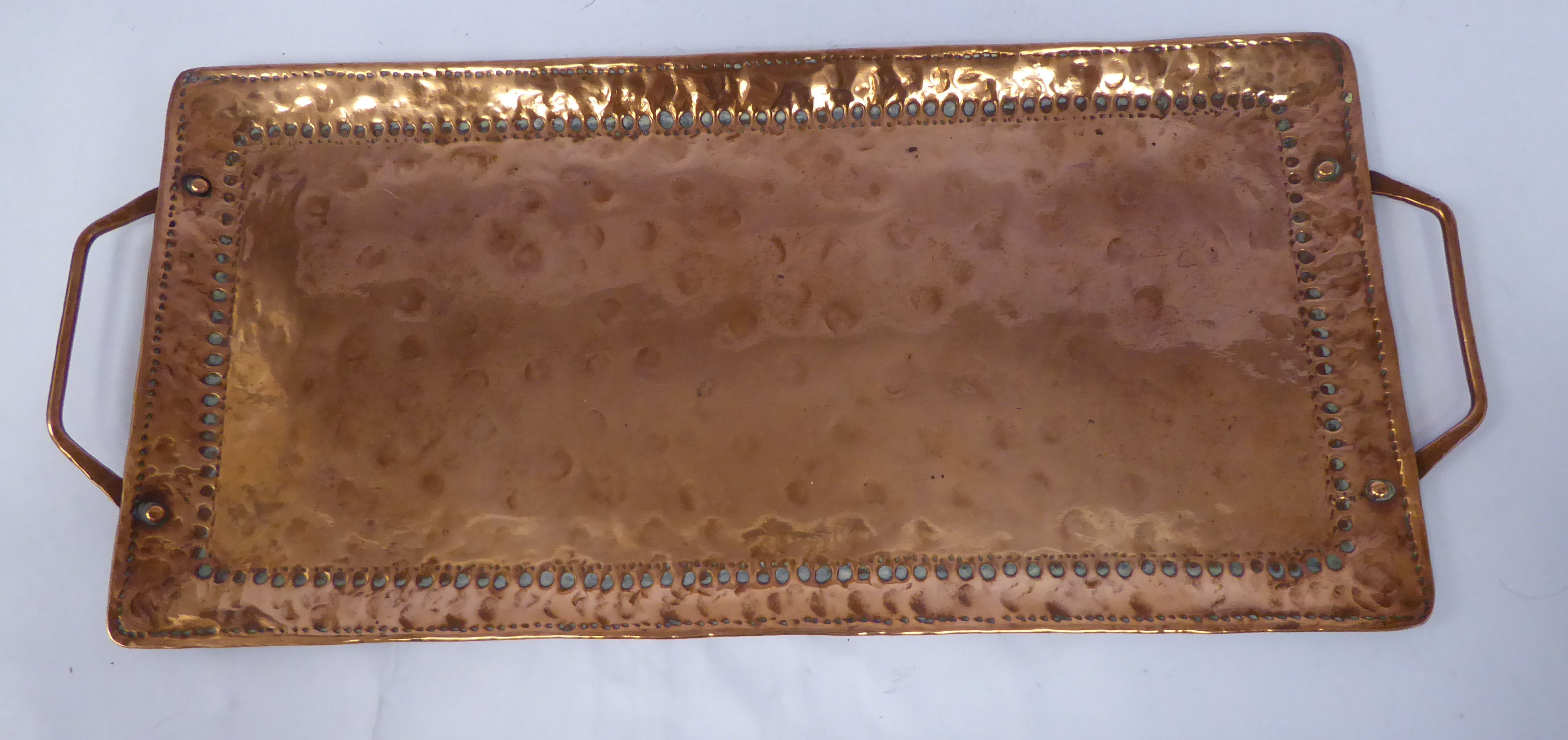 An Arts & Crafts twin handled copper tray with spot-hammered decoration to the border bearing the