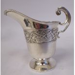 A silver cream jug of helmet design with a C-scrolled handle and band of embossed Celtic inspired