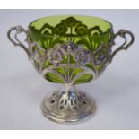 An Art Nouveau EPNS twin handled pedestal cup with a tinted green glass liner,