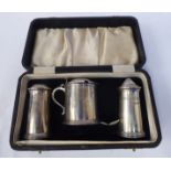 A silver three piece condiments set comprising a tall, tapered, cylindrical pepper and salt pot,