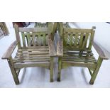 A pair of modern teak garden chairs, each with a slatted back and seat,