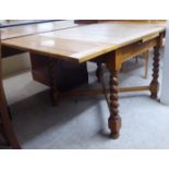 A 1920s light oak draw leaf dining table, the top raised on barleytwist block legs,