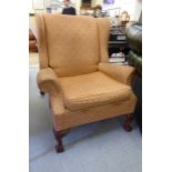 A mid 20thC Georgian inspired upholstered wingback armchair with a cushion seat, raised on stubby,