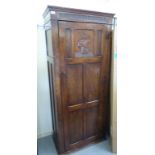 A 1930s stained oak hallrobe with a moulded cornice, over a panelled door, enclosing a single rail,