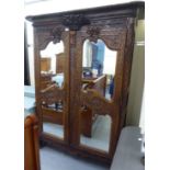A 19thC oak armoire, the frieze carved with a floral spray, over a pair of mirrored doors,
