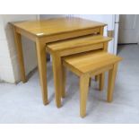 A nesting set of three modern light oak occasional tables, raised on square,