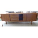 A 1970s teak sideboard with an arrangement of three sliding doors and an offset bank of four