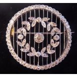 A white gold coloured metal and diamond set wheel brooch