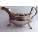 A silver sauce boat with a decoratively cast and flared rim and a hollow C-scrolled handle,