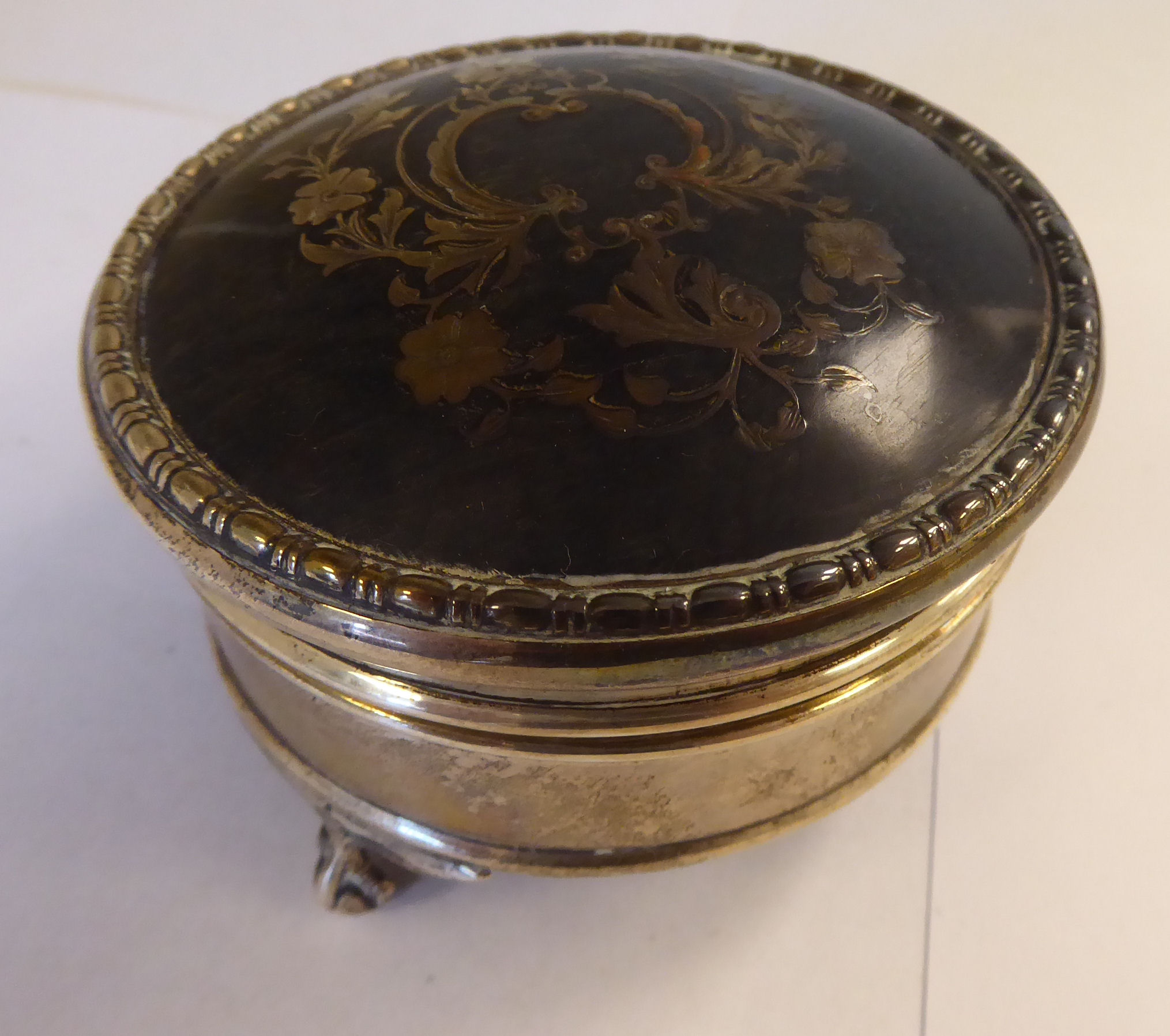 A silver circular ring box with a piquetworked tortoiseshell panel on the hinged lid,